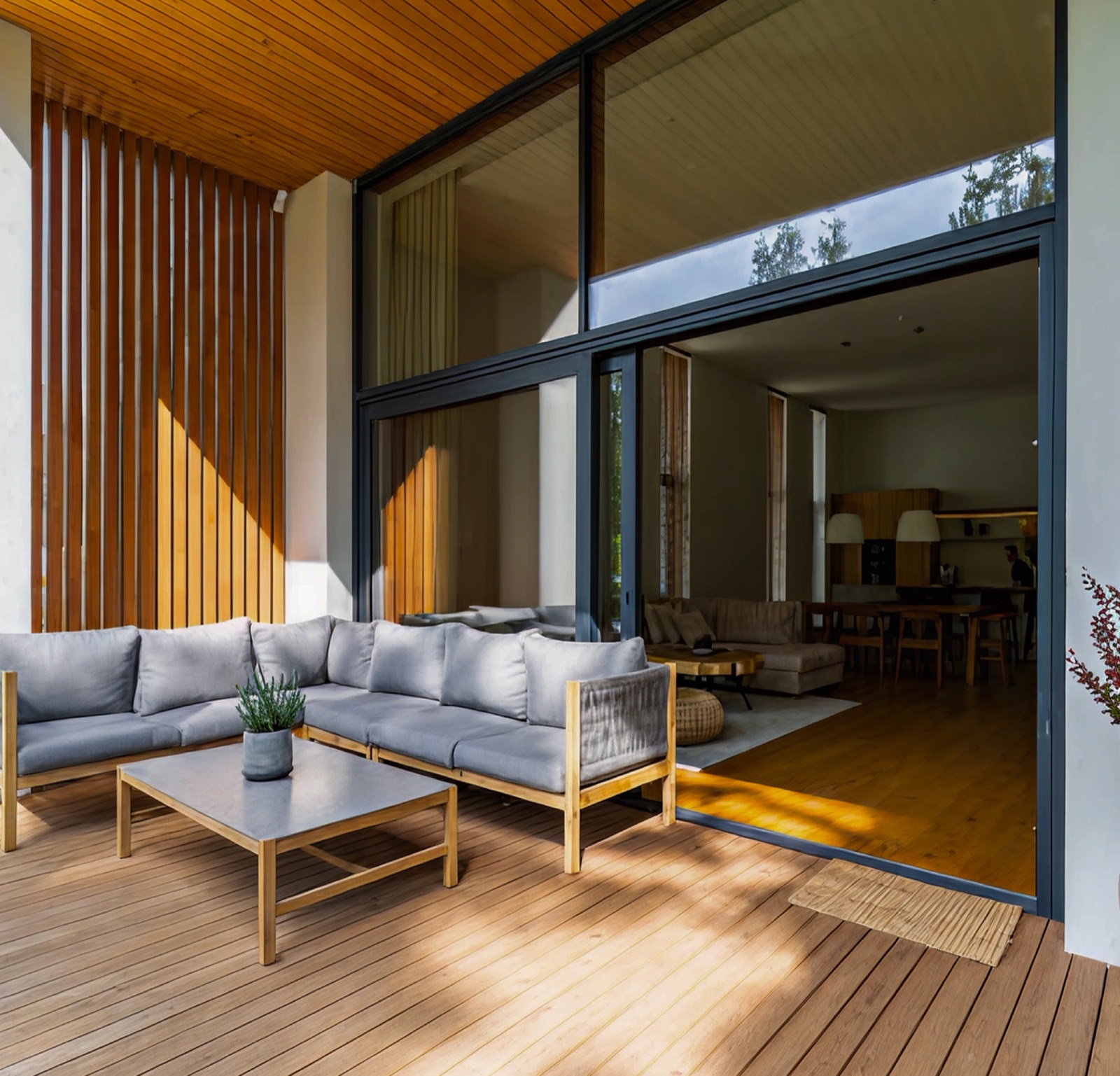 Floor-to-ceiling timber-framed glazing opening onto a sunlit terrace