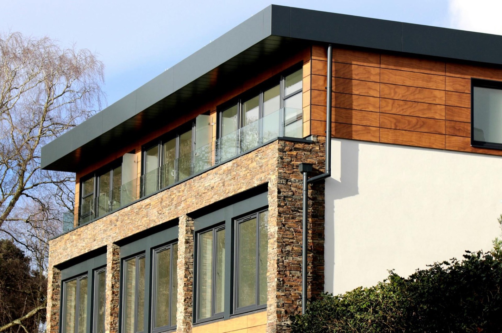 Contemporary home with dark-framed timber glazing above stone-clad walls