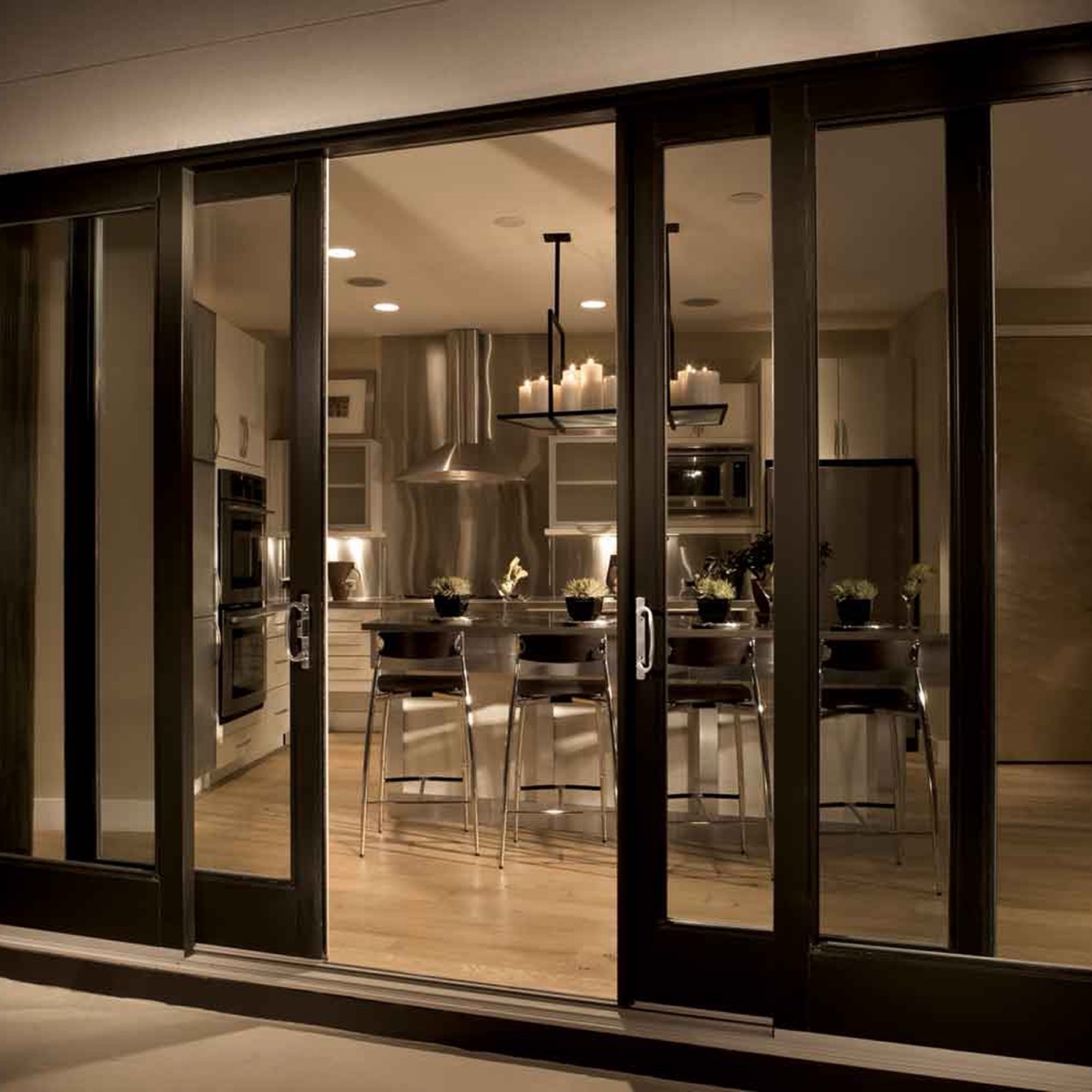 Black-framed sliding glazed doors looking into a warmly lit kitchen